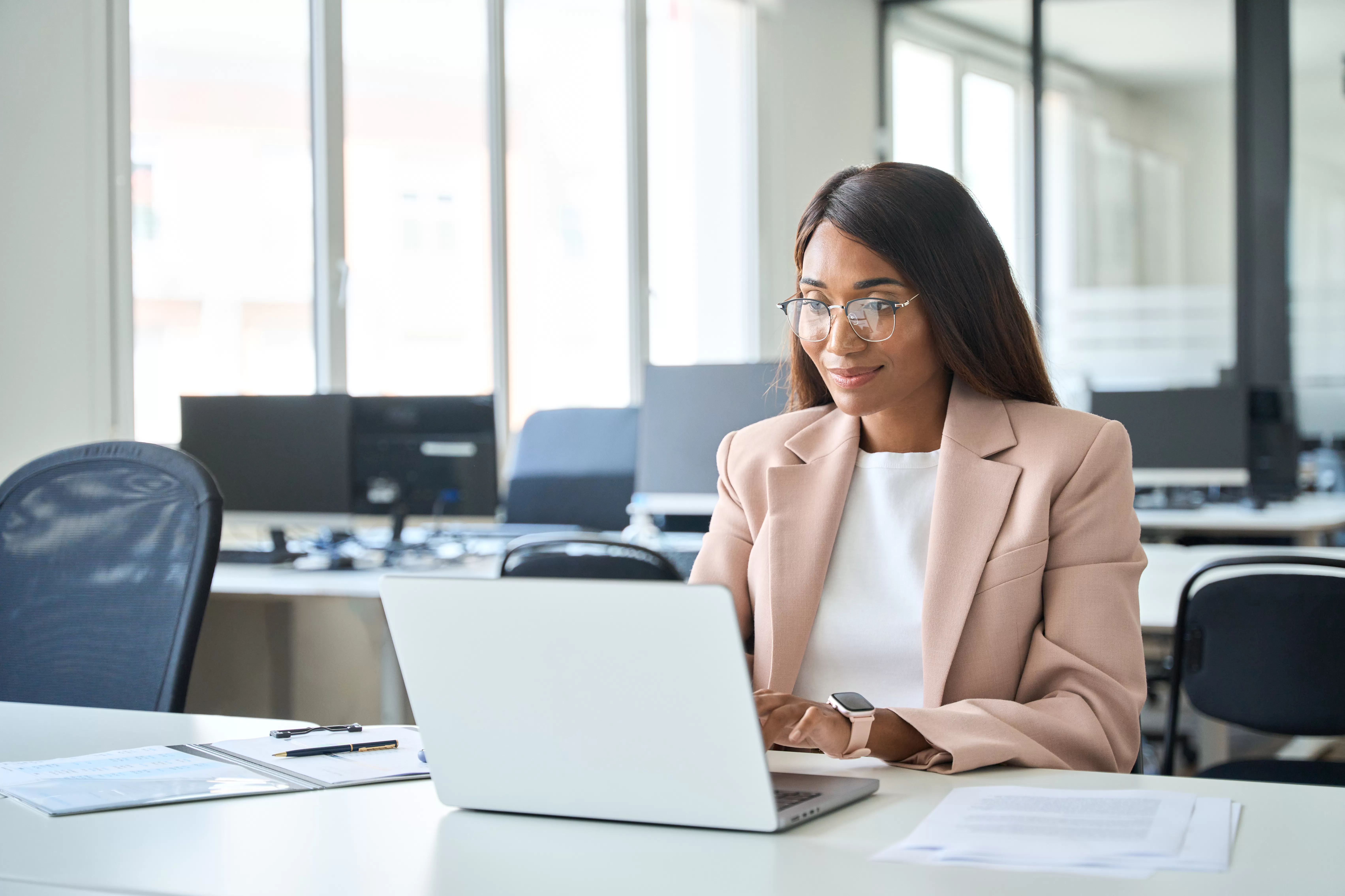 HR professional working on a laptop at a desk in a modern office environment.