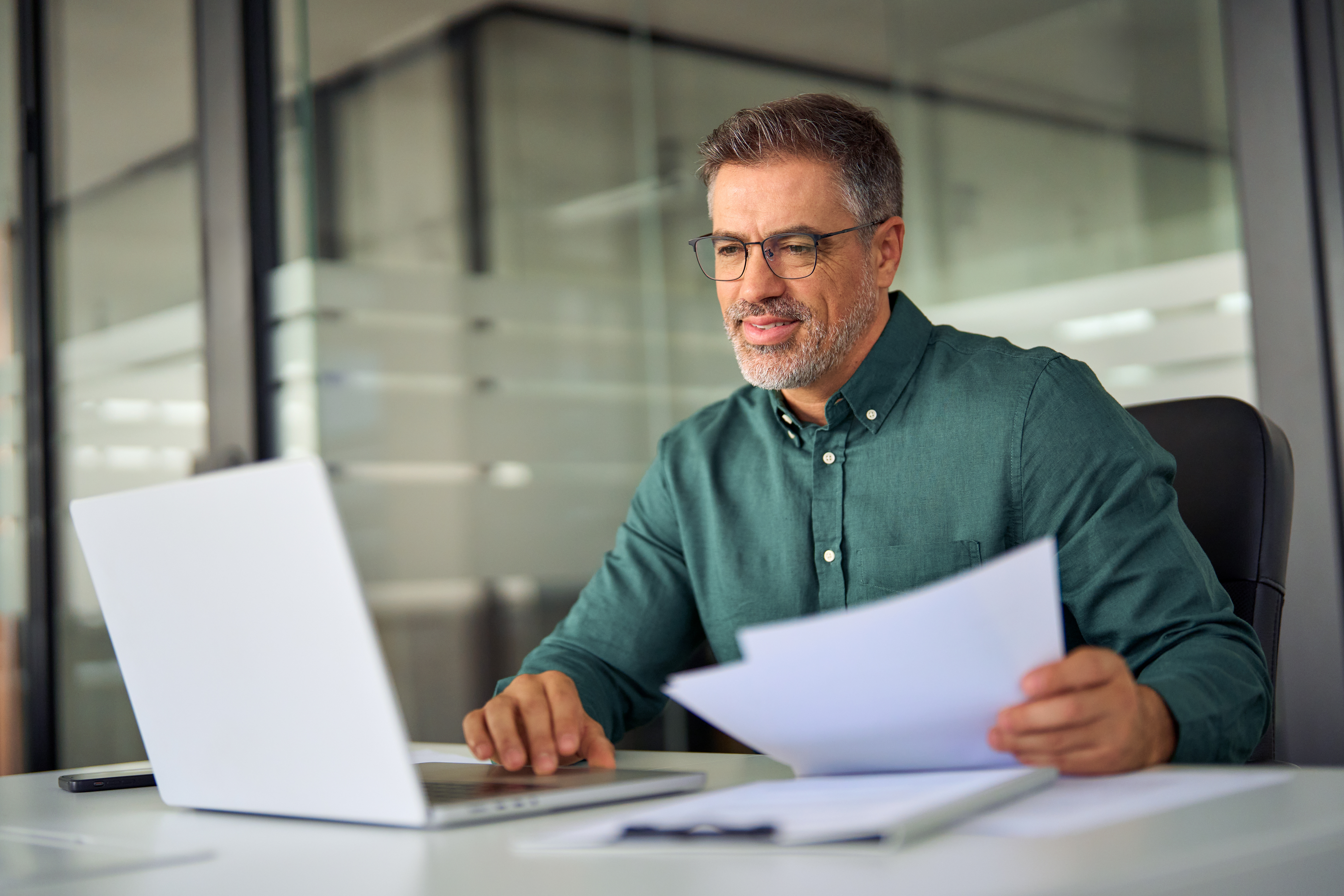 Male HR professional reviewing documents while working on a laptop in a modern office.