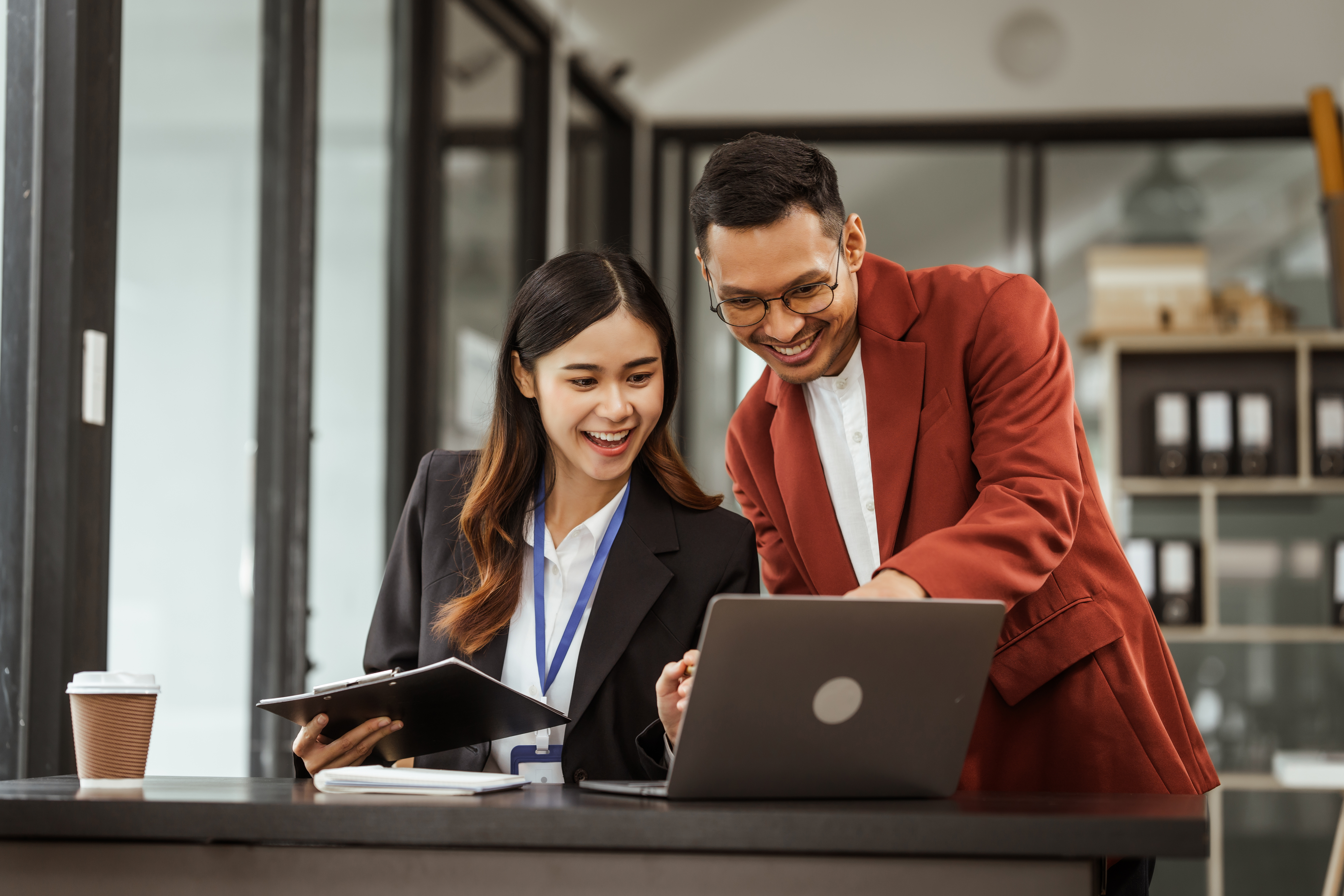 Male and female professionals reviewing information together on a laptop while standing at a desk in a modern office.